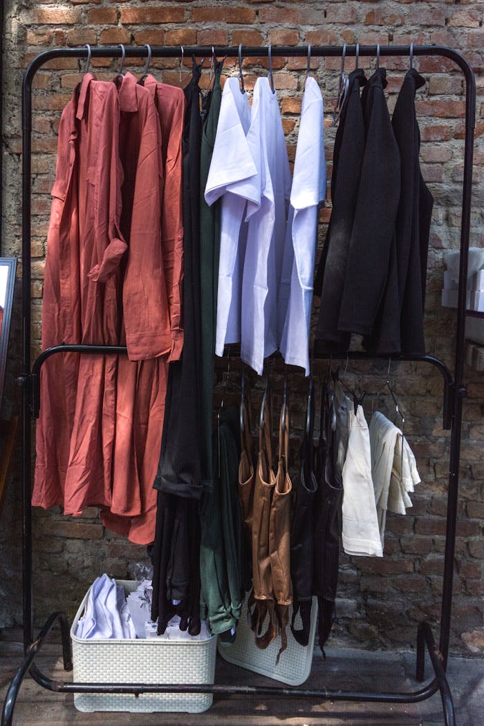 A diverse collection of garments neatly hung on a clothing rack against a rustic brick wall, showcasing fashion variety.